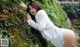 A woman in a white shirt leaning against a moss covered rock.