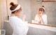 A woman in a white robe brushing her teeth in front of a mirror.