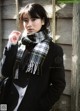 A woman wearing a black coat and a plaid scarf.