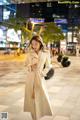 A woman in a white trench coat is walking down the street.